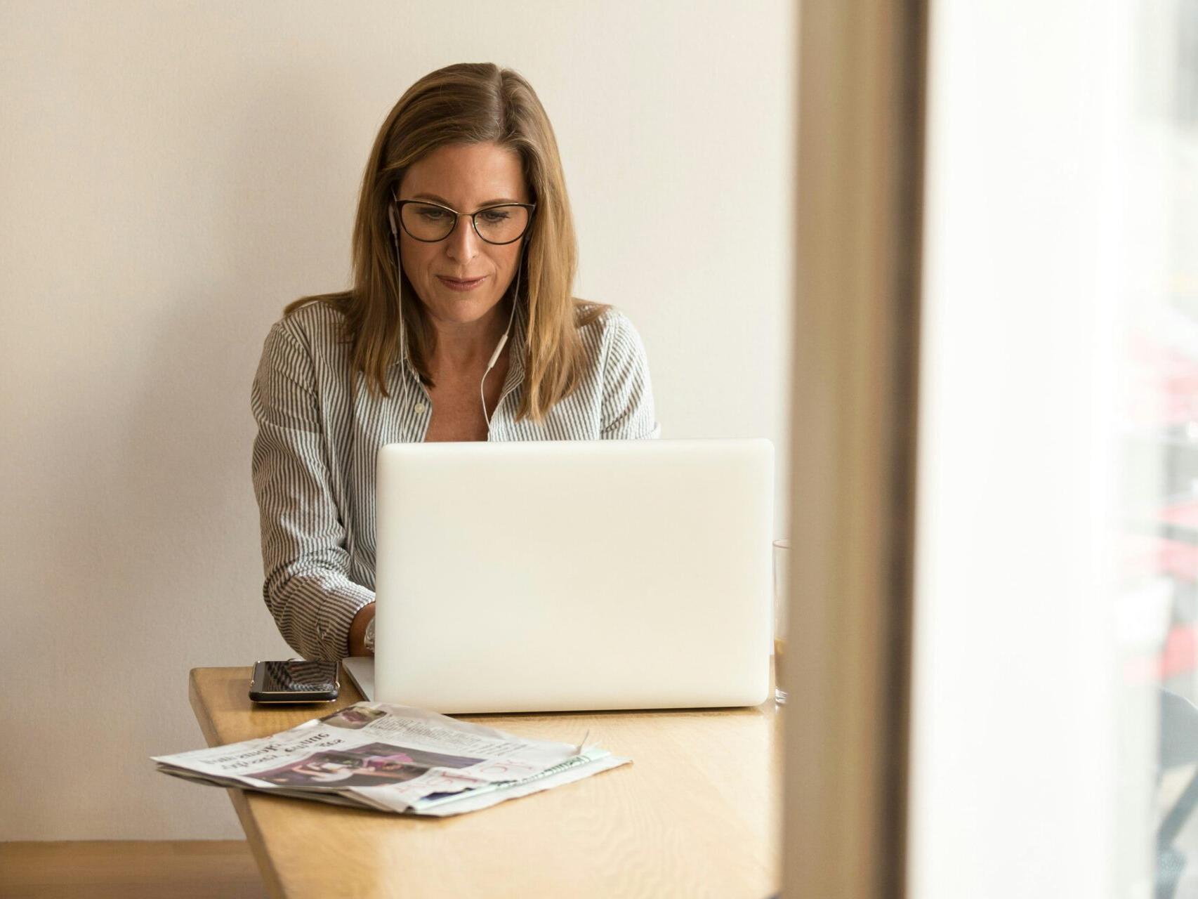 戴眼镜的女人坐在桌子旁用笔记本电脑